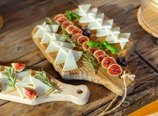 Slices of delicious cheese for degustation, served with figs and rosemary on a wooden table in...