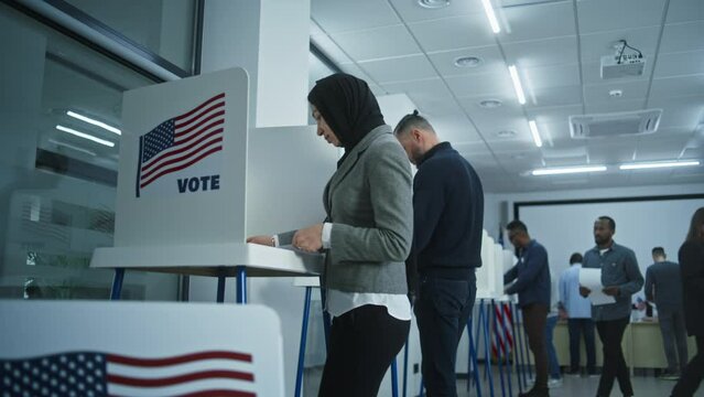 Arabic female American citizen votes in booth in polling station office. National Elections Day in United States. Political races of US presidential candidates. Concept of patriotism and civic duty.