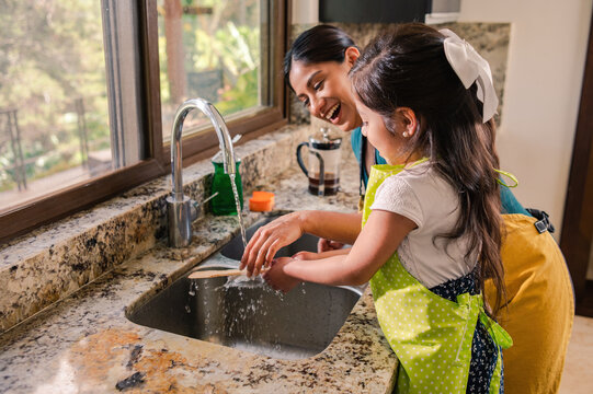 Latin Mother and Daughter. The mother teaches her daughter to wash the dishes they share moments together and have fun.