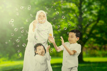 Young Muslim mother playing soap bubbles with their children in the garden