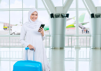 Happy Asian muslim woman carrying a suitcase and holding phone