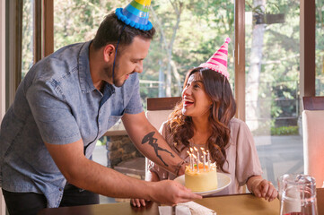 Husband brings a cake to the table to celebrate his wife's birthday.