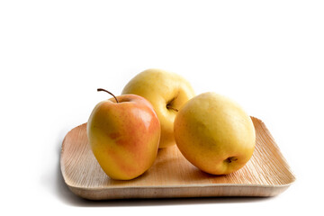 Three golden delicious apples on a wooden plate isolated on white

