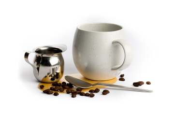 a stainless steel creamer and spoon with a coffee cup and coffee beans isolated on white