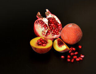 Pieces of a ripe peach and a broken pomegranate fruit with scattered seeds on a black background.