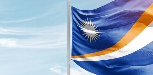 Marshall Islands national flag with mast at light blue sky.