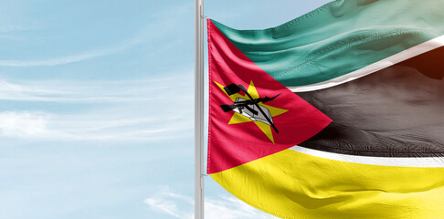 Mozambique national flag with mast at light blue sky.