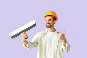 Male decorator with putty knife showing thumb-up on lilac background
