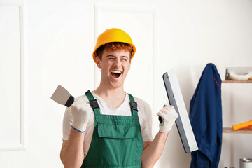 Male decorator with putty knives working in room
