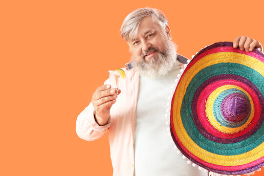 Portrait of senior man with shot of tequila and colorful sombrero on orange background