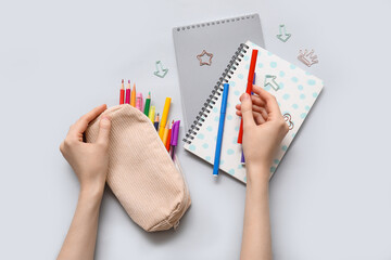 Child's hands with pencil case, different school stationery and notebooks on grey background