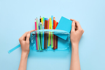 Child's hands with pencil case, different school stationery and notebook on blue background