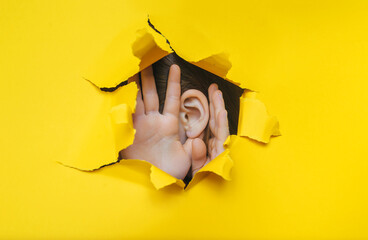 Female ear and hand close-up. Copy space. Torn paper, yellow background. The concept of...