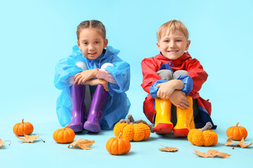 Little children in rubber boots with pumpkins and autumn leaves on blue background