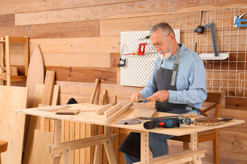 Mature carpenter working with wooden plank at table in shop