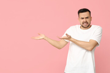 Handsome worried young man showing something on pink background