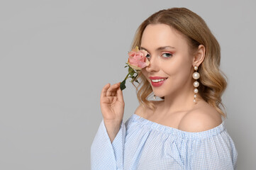 Happy young woman with beautiful rose on grey background