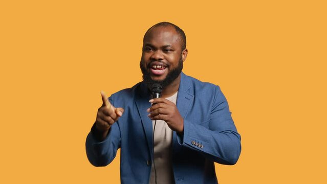 African american motivational speaker holding monologue using microphone, gesturing with hands, studio background. Energetic BIPOC speaker talking during presentation using mic, doing speech, camera A