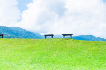 Wooden bench in green grass on slope with clouds and blue sky,Beautiful green hills, pastures and trees,space for text,copy space.