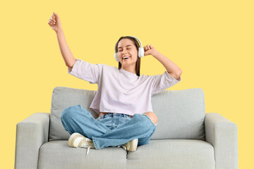 Beautiful young woman in headphones resting on sofa and listening music against yellow background