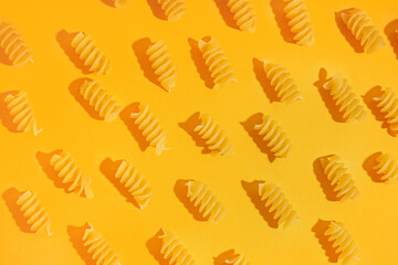 Composition with uncooked fusilli pasta on orange background