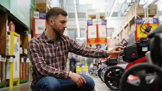 A man in garden center of hardware store chooses lawn mower