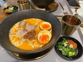 A bowl of Japanese Tonkotsu Ramen with egg, smoked beef and spicy creamy broth. Served with green tea and some garnish