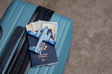 A US citizen passport and American dollars lie next to a model airplane on a travel baggage.