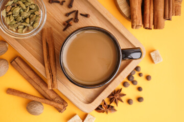 Cup of tasty masala tea with different spices on yellow background, closeup