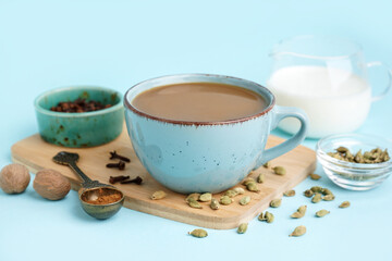 Cup of tasty masala tea with different spices on blue background, closeup