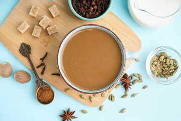 Cup of tasty masala tea with different spices on blue background