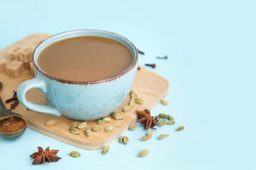 Cup of tasty masala tea with different spices on blue background, closeup