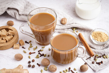 Glass cups of tasty masala tea with different spices on light background