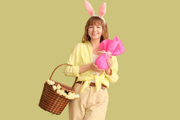 Young girl with Easter bunny ears, basket and gift on color background