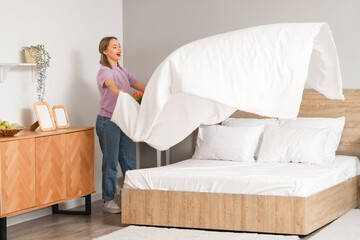 Pretty young woman making bed in modern bedroom