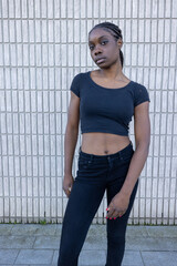 In this portrait, a young African woman stands against a textured brick wall, projecting a cool and...