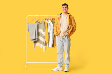 Handsome young happy man and rack with stylish clothes on yellow background