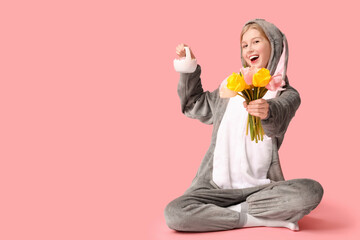 Beautiful young happy woman in bunny costume with tulips and basket on pink background. Easter...