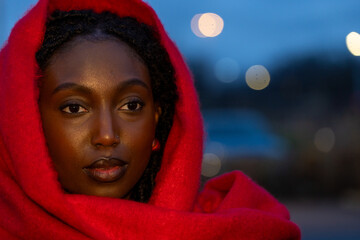 This evocative portrait features a young woman wrapped in a vibrant red scarf, her gaze penetrating...