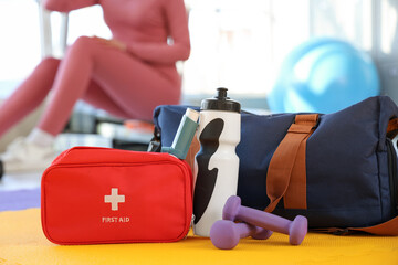 First aid kit with inhaler, dumbbells and sports bag in gym, closeup
