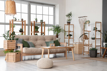 Interior of spacious living room with sofa, table, houseplants, shelving units and window