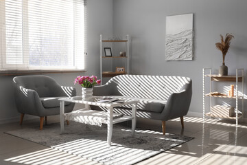 Interior of light living room with sofa, armchair and tulips on table
