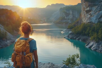 A traveler stands overlooking a serene lake and mountains at sunrise, back to the viewer.