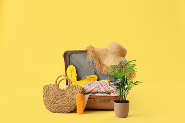 Open suitcase with beach accessories and palm on yellow background