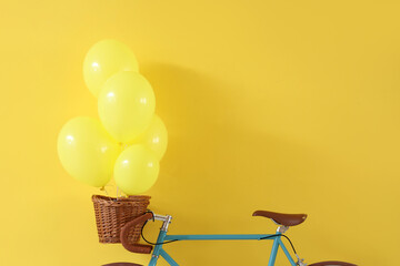 Bicycle with balloons in basket on yellow background