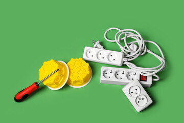 Extension cords, electrical junction boxes and screwdriver on green background