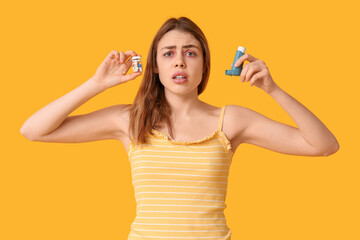 Young woman with jar of pills and inhaler on yellow background