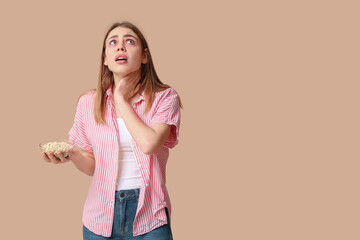 Young woman with bowl of nuts suffering from allergy on brown background