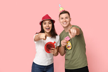 Young friends in funny disguise with paper stickers and whoopee cushion pointing at viewer on pink background. April fool's day celebration