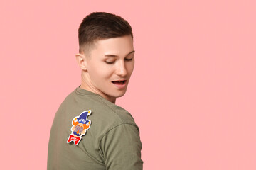 Handsome young shocked man with paper clown attached to his back on pink background. April fool's...